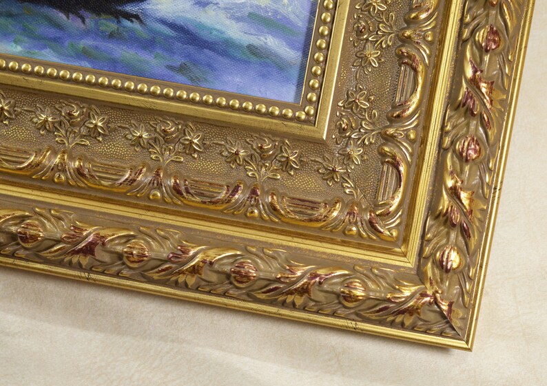 May include: A gold-colored picture frame with ornate detailing. The frame has a raised edge and a textured surface. The frame is made of wood and has a dark brown finish.