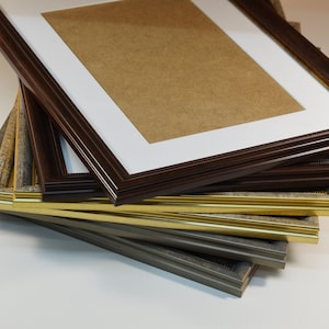 May include: A stack of picture frames in various colors and styles, including brown, gold, and gray. The frames are made of wood and have a variety of decorative details.