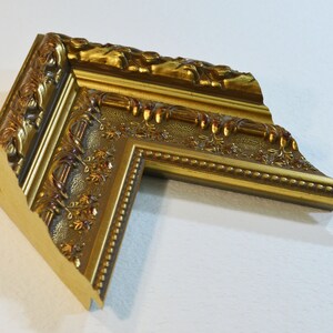 May include: A gold picture frame with ornate details and a beaded edge.