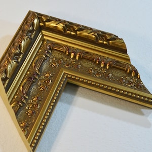 May include: A gold picture frame with ornate detailing and a beaded edge. The frame is made of wood and has a distressed finish.