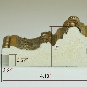 May include: A close-up of a white picture frame with gold accents. The frame is 2 inches tall, 4.13 inches wide, and 0.57 inches deep.