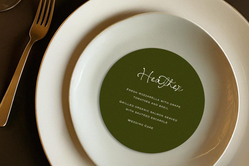 May include: A formal place setting with a gold fork and white plates with gold rims. A green circular menu card with the name "Heather" and a list of menu items is centered on the plate.