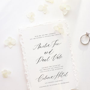 May include: A wedding invitation with a white background and delicate white flowers scattered around the edges. The invitation is for the wedding of Amelia Fox and Paul Vale, to be held on Saturday, May 10th, 2021 at 5:00 PM at the Celosia Hotel in Los Angeles, California.