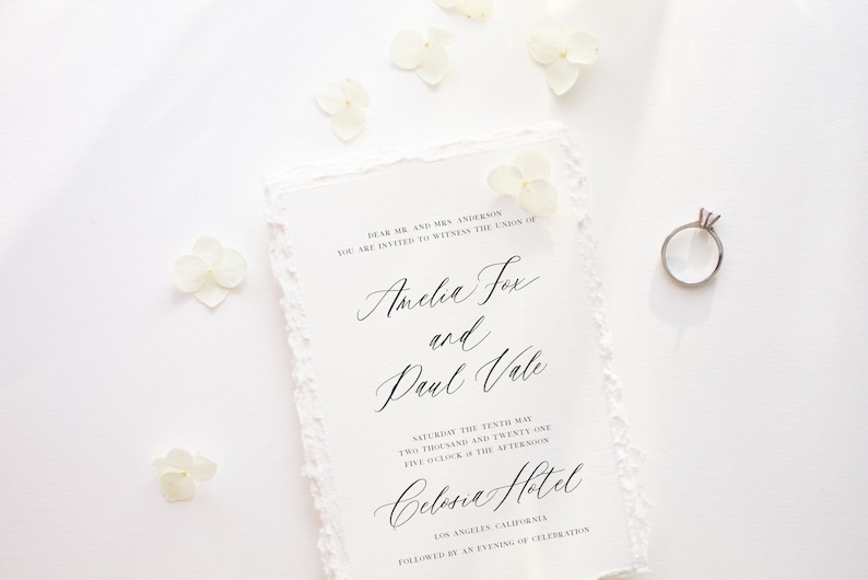 May include: A wedding invitation with a white background and delicate white flowers scattered around the edges. The invitation is for the wedding of Amelia Fox and Paul Vale, to be held on Saturday, May 10th, 2021 at 5:00 PM at the Celosia Hotel in Los Angeles, California.