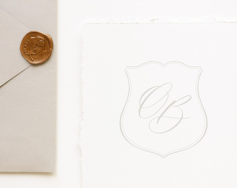 Puede incluir: Una tarjeta blanca con una forma de escudo gris y las iniciales "OB" escritas en cursiva dentro del escudo.