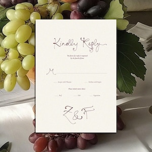 May include: A cream-colored wedding reply card with the words "Kindly Reply" in elegant script. The card includes spaces for guest names, menu choices, and initials. The card is set on a table with grapes, glassware, and a candle.