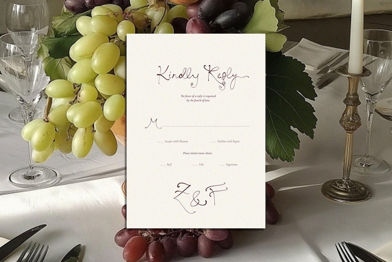 May include: A cream-colored wedding reply card with the words "Kindly Reply" in elegant script. The card includes spaces for guest names, menu choices, and initials. The card is set on a table with grapes, glassware, and a candle.