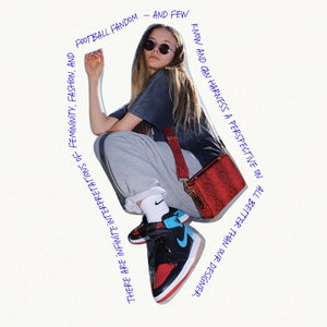 May include: A woman wearing a gray sweatshirt, black t-shirt, and black and red sneakers with a blue accent. She is carrying a red crossbody bag with a black strap. The image has text that reads "FOOTBALL FANDOM - AND FEW KNOW AND CAN HARNESS A PERSPECTIVE ON ALL BETTER THAN OUR DESIGNER. THERE ARE INFINITE INTERPRETATIONS OF FEMININITY, FASHION, AND"
