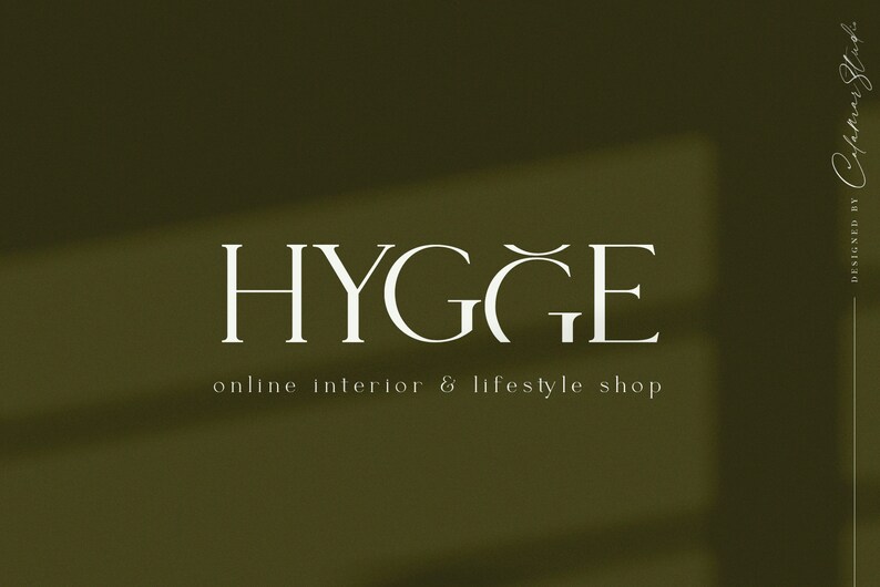 K&ouml;nnte beinhalten: Wei&szlig;er Text auf gr&uuml;nem Hintergrund lautet "HYGGE" mit einer Tilde &uuml;ber dem "G". Unter dem Text steht "Online-Shop f&uuml;r Innenarchitektur & Lifestyle". Der Text wurde von "Cypria Studio" entworfen.
