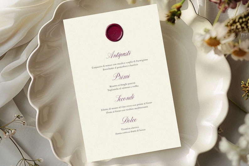 May include: A cream-colored menu card with a burgundy wax seal, featuring Italian text. The menu is placed on a white, scalloped-edge plate, with floral accents. The menu lists antipasti, primi, secondi, and dolce.