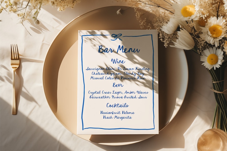 May include: A white bar menu with blue handwritten text. The menu lists wine, beer, and cocktails. The text includes: Sauvignon Blanc, Dr. Loosen Riesling, Chateau d'yquem, Cloudy Bay, Miroval Cotes de Provence Rose, Crystal Clear Lager, Amber Waves, Fairweather Nuova Fruited Sour, Passionfruit Paloma, and Peach Margarita.