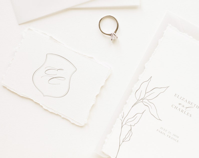 Puede incluir: Un conjunto de invitaciones de boda con un dise&ntilde;o simple y elegante. La invitaci&oacute;n presenta una ilustraci&oacute;n floral dibujada a mano y el texto "Elizabeth y Charles" con la fecha "21 de julio de 2020" y la ubicaci&oacute;n "Par&iacute;s, Francia". La tarjeta RSVP presenta un monograma con las iniciales "EC" en forma de escudo.