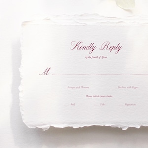 May include: A white invitation card with a deckled edge, featuring the words "Kindly Reply" in burgundy script. The card includes prompts for the recipient to respond, with options for meal choices.