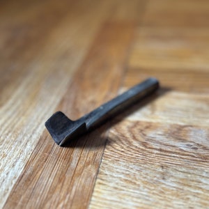 May include: A black metal tool with a curved blade, lying on a wooden surface.