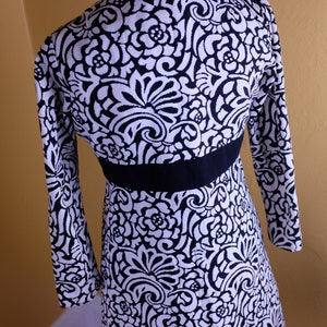 K&ouml;nnte beinhalten: Ein schwarz-wei&szlig;es Kleid mit Blumenmuster. Das Kleid hat lange &Auml;rmel und einen taillierten Oberteil. Das Kleid ist aus einem weichen, dehnbaren Stoff.