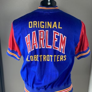 May include: A blue and red short-sleeved jacket with the text "ORIGINAL HARLEM GLOBETROTTERS" embroidered on the back. The jacket has yellow, red, and white stripes around the collar and bottom.
