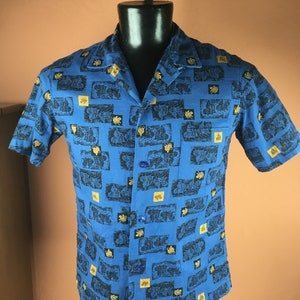 May include: A blue short-sleeved button-down shirt with a repeating pattern of black and gold stylised images.