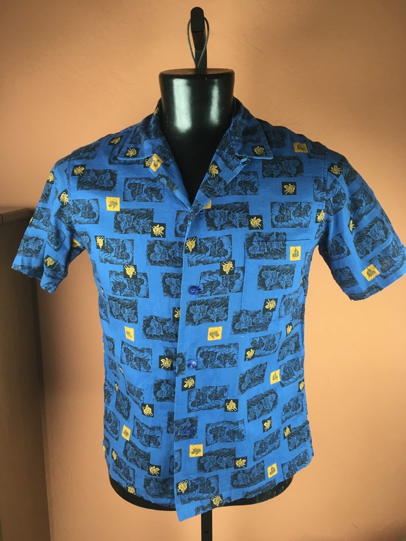 May include: A blue short-sleeved button-down shirt with a repeating pattern of black and gold stylised images.