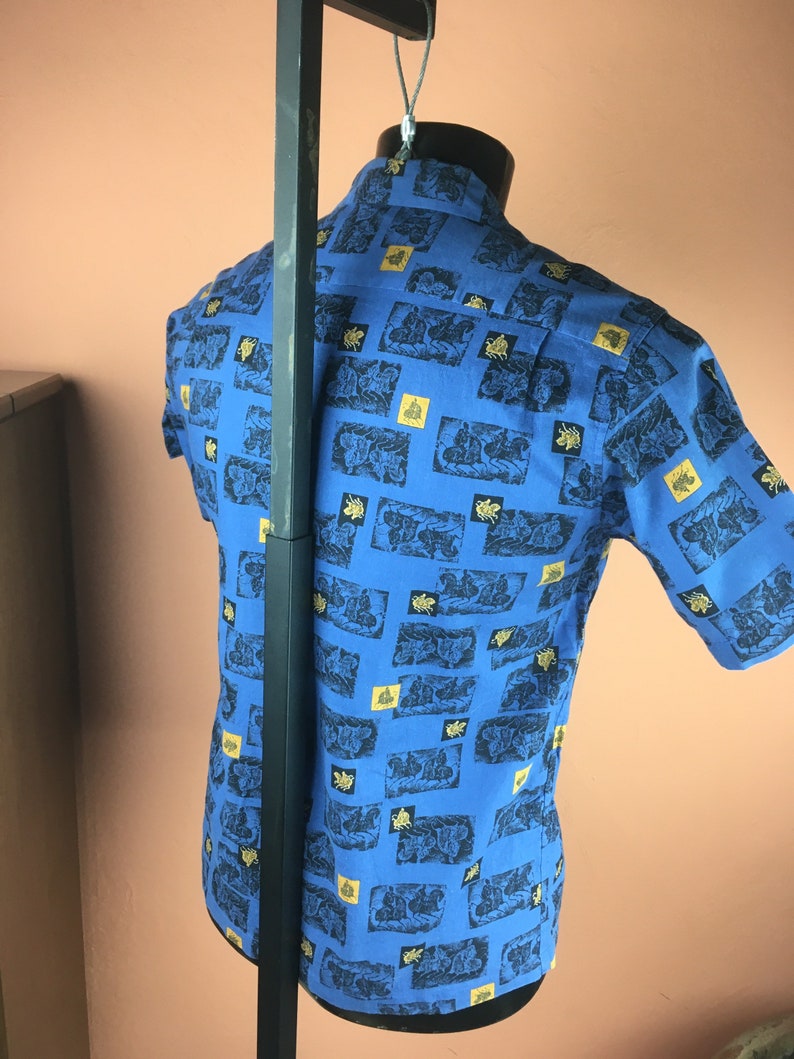 May include: A blue short-sleeved shirt with a pattern of gold and black figures on a white background.