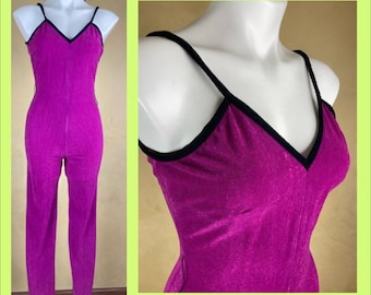 May include: A vibrant fuchsia jumpsuit with a V-neckline and spaghetti straps, trimmed in black. The one-piece garment is displayed on a mannequin, showcasing its form-fitting silhouette and textured fabric. The jumpsuit has a sleek, modern design.