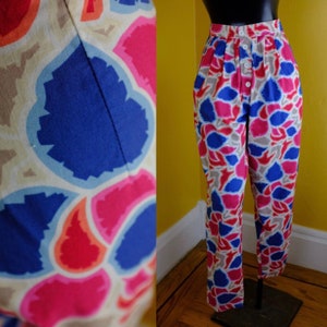 May include: High-waisted pants with a colorful abstract print featuring shades of blue, pink, red, and beige. The pants have a button closure and are made of a lightweight fabric.