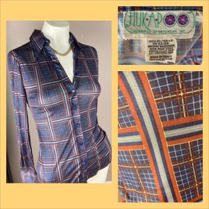 Puede incluir: Una camisa de manga larga con botones y cuello, con un patrón geométrico en tonos azules y naranjas. La camisa está hecha de 100% poliéster y tiene una etiqueta que dice "HUKAPOO SPORTSWEAR INC. 100% POLYESTER RN 34104 MACHINE WASH WARM WITH MILD SOAP DRY LOW  MADE IN TAIWAN REPUBLIC OF CHINA".