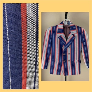 May include: A double-breasted blazer with vertical stripes in navy blue, red, and white. The jacket has a notched lapel, two rows of buttons, and two front pockets. The fabric has a textured appearance.