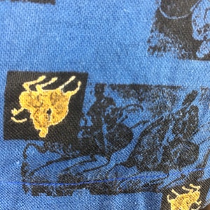 May include: Blue fabric with a repeating pattern of black and gold silhouettes of people riding horses. The fabric has a blue seam along the bottom edge.