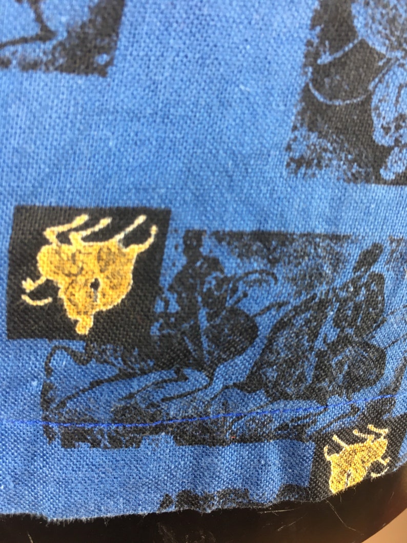 May include: Blue fabric with a repeating pattern of black and gold silhouettes of people riding horses. The fabric has a blue seam along the bottom edge.