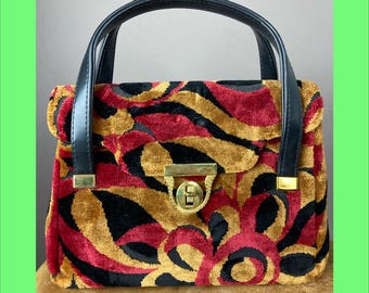 Puede incluir: Bolso de mano vintage con asa negra y cierre dorado. El bolso presenta un vibrante estampado de terciopelo rojo, dorado y negro. El bolso tiene forma rectangular con cierre de solapa y diseño estructurado.