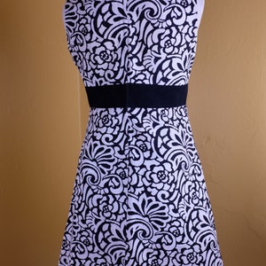 K&ouml;nnte beinhalten: Ein &auml;rmelloses schwarz-wei&szlig;es Kleid mit Blumenmuster. Das Kleid hat einen schwarzen Tailleng&uuml;rtel und ein figurbetontes Oberteil.
