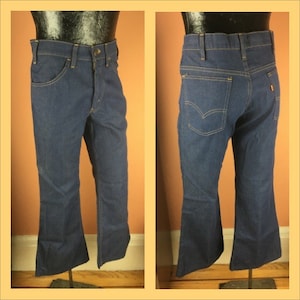 Puede incluir: Un par de pantalones vaqueros de campana de mezclilla azul oscuro con pierna recta y una amplia campana en la parte inferior. Los vaqueros tienen un diseño clásico de cinco bolsillos y cierre de botón.