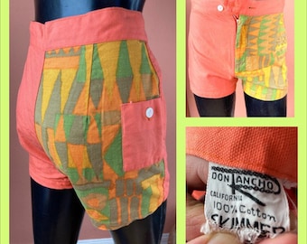 May include: Orange and green patterned swim trunks with a side pocket and a label that reads "Don Ancho California 100% Cotton Skimmer."