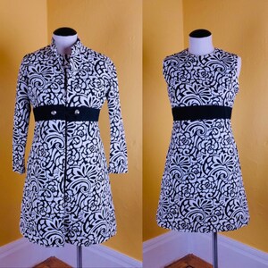 K&ouml;nnte beinhalten: Ein schwarz-wei&szlig; gemustertes Kleid mit einem schwarzen G&uuml;rtel und einer passenden Jacke. Das Kleid und die Jacke haben ein florales Design.