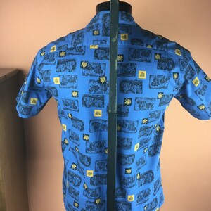 May include: A blue short-sleeved shirt with a repeating pattern of black and gold images. The shirt is on a mannequin.