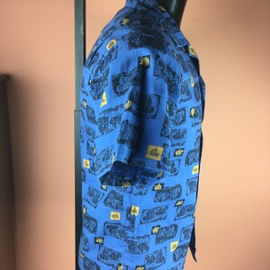 May include: A blue short-sleeved button-down shirt with a gold and black patterned design.