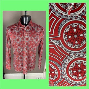 May include: A long-sleeve button-down shirt with a vibrant red and white geometric pattern. The shirt is displayed on a black mannequin. The pattern includes circular and cross-like shapes. The fabric appears to be a lightweight material.