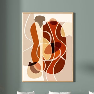 May include: Abstract art print featuring a brown, orange, and beige colour scheme. The print depicts a large, organic shape with smaller shapes and lines within it. The print is framed in a light wood frame and is hanging on a sage green wall.