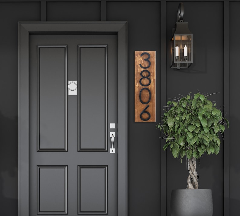 May include: A black front door with a wooden house number plaque that reads "3806" mounted on the wall next to the door. A black light fixture with two bulbs is mounted above the door.