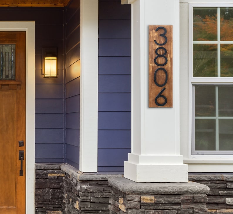 May include: A wooden house number sign with black metal numbers. The sign is mounted on a white column and reads "3806".
