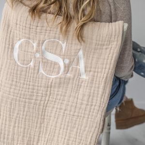 May include: A beige muslin baby blanket with the monogram "C.S.A." embroidered in white.