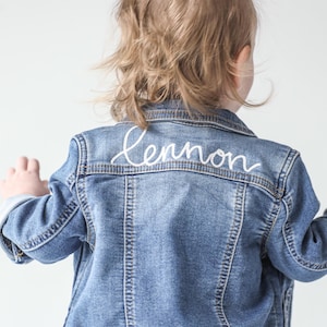 May include: A blue denim jacket with the name "Lennon" embroidered in white on the back.