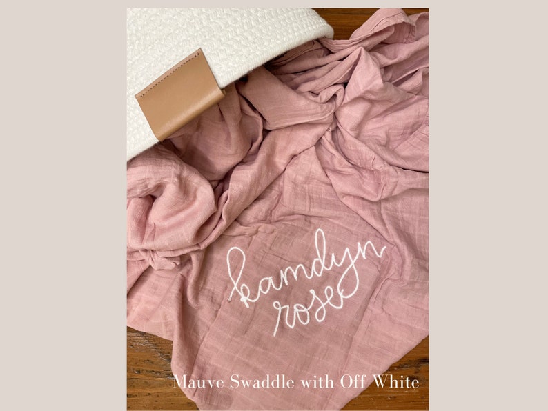 K&ouml;nnte beinhalten: Ein mauvefarbenes Musselin-Swaddle-Decken mit dem Namen "Kamdyn Rose" in wei&szlig; gestickt.