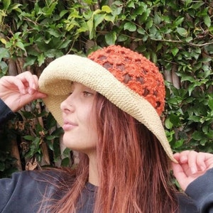 Puede incluir: Una persona con una sudadera negra y un sombrero de sol de crochet marrón y naranja.