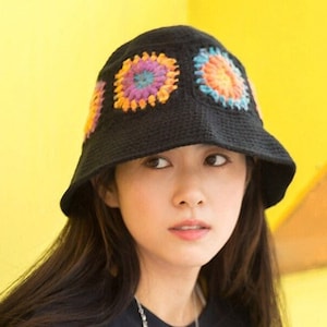 Könnte beinhalten: Ein schwarzer Bucket-Hut mit bunten gehäkelten Blumen auf der Krone.