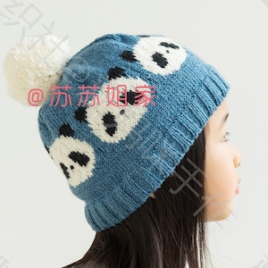 May include: A blue knitted hat with a white pom pom and panda bear designs. The hat is worn by a child with long black hair.