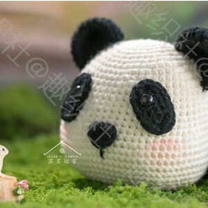 close up view of left side of head of crochet panda amigurumi, panda head lying on grassy ground with his chin, staring tiny rabbit resting on miniature stump, panda pupils made of buttons, with outdoor garden background