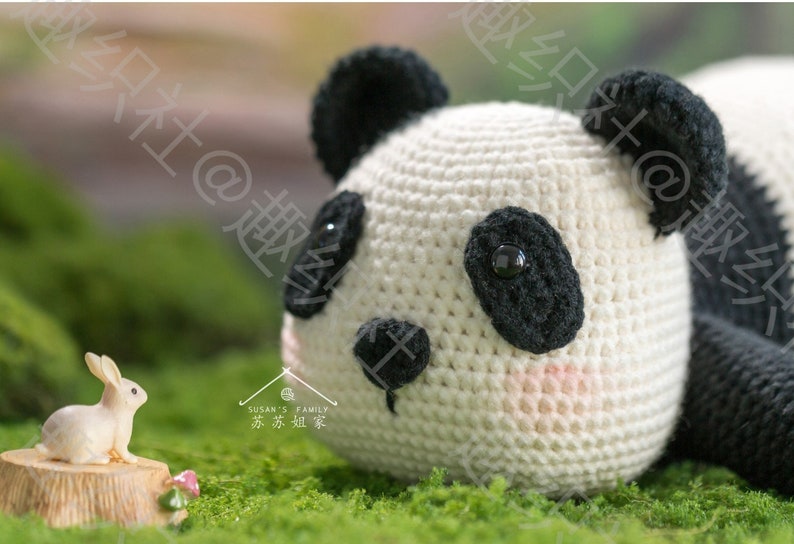 close up view of left side of head of crochet panda amigurumi, panda head lying on grassy ground with his chin, staring tiny rabbit resting on miniature stump, panda pupils made of buttons, with outdoor garden background