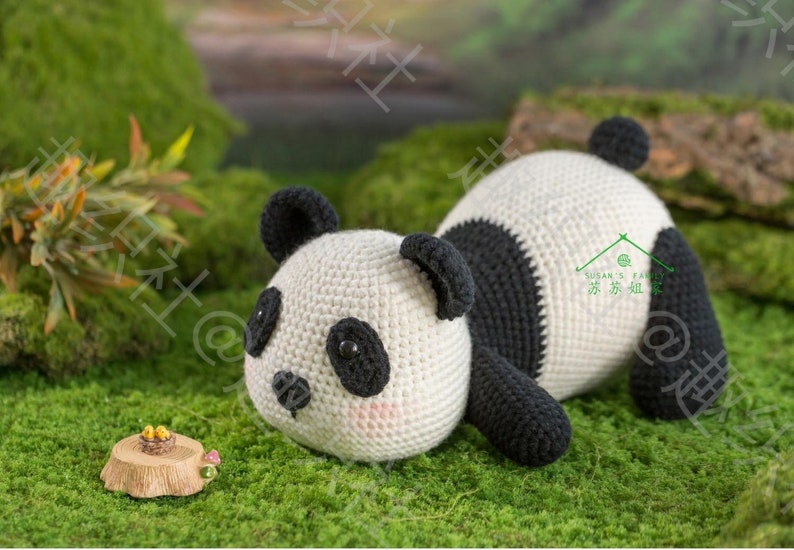 45 degree left front view of panda amigurumi/plushie toy/doll lying with chin on grassy ground, panda watching sth. tiny in front him, his limb, tummy and chin all resting on ground, with hip rising up high in air, with garden background