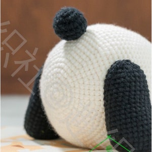 close up detailed 45 degree view of the right side of butt of crochet panda plushie amigurumi, panda's white butt is very round with ball shaped black tail stuck on butt, two short chungky legs at both sides, panda resting on colored table